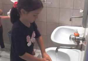 Marta ćwiczy prawidłowe mycie rąk przy umywalce.